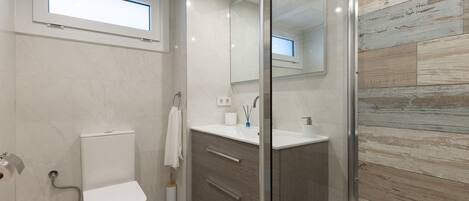 A modern bathroom with a toilet, sink, vanity, and a glass shower enclosure.