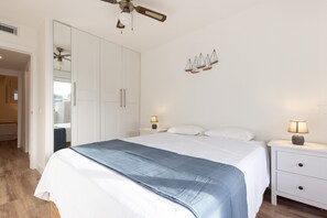 A bedroom with a bed, white nightstands, a ceiling fan, and a wall-mounted scale decoration.