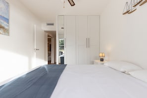 Un dormitorio con una cama, una mesita de noche con lámpara, un armario y un cuadro en la pared.