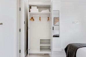 A white closet with shelves, hanging space, and a bed with a patterned blanket. - Bright Modern Flat Marylebone (London)
