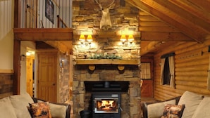 A log cabin interior with a stone fireplace, two sofas, a wooden coffee table, and a ceiling with wooden beams.