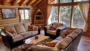 A log cabin interior with a sofa set, a coffee table, a bookshelf, and a painting on the wall.