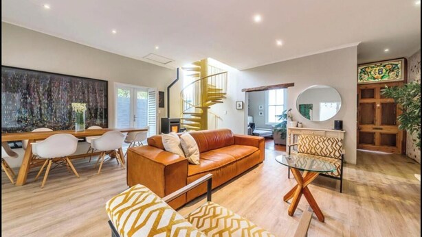 A modern living room with a spiral staircase, a dining area with a wooden table and chairs, and a sofa with patterned cushions. - 3 Bedroom Home in Gardens Cape Town (Cape Town)