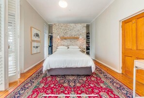 Ein Schlafzimmer mit einem Bett, einem gemusterten Teppich, einer Ziegelwand und einer Holztür.