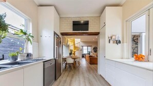 A modern kitchen with a dishwasher, a dining area with a table and chairs, a staircase leading to an upper level, and a flat-screen TV mounted on the wall. - 3 Bedroom Home in Gardens Cape Town (Cape Town)