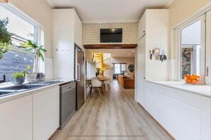 Una cocina moderna con lavavajillas, un comedor con mesa y sillas, una escalera que sube a un nivel superior y un televisor de pantalla plana montado en la pared.