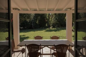 A covered patio with a table and chairs, overlooking a grassy area with trees. - CABRA - Bear House (Setúbal)