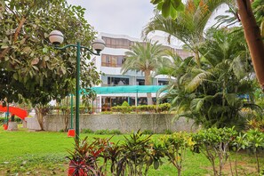 A building with a green roof, surrounded by lush greenery and a red structure in the background.