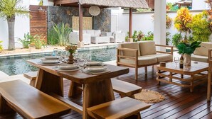 An outdoor dining area with wooden tables and benches, a pool, and lounge chairs. - Stunning Latanier villa-private pool in Grand Bay (Rivière du Rempart District)