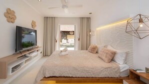 A modern bedroom with a large bed, a television on a wooden console, and a view of an outdoor pool. - Stunning Latanier villa-private pool in Grand Bay (Rivière du Rempart District)