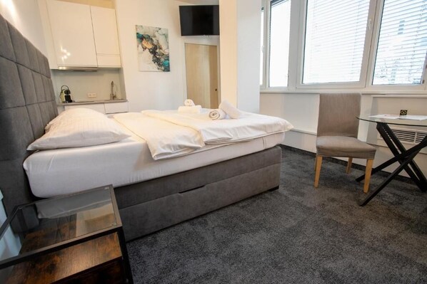 A modern hotel room with a bed, a small table, a chair, a TV, and a window. - Cube Apartments by Wiener Stadthalle (Vienna)