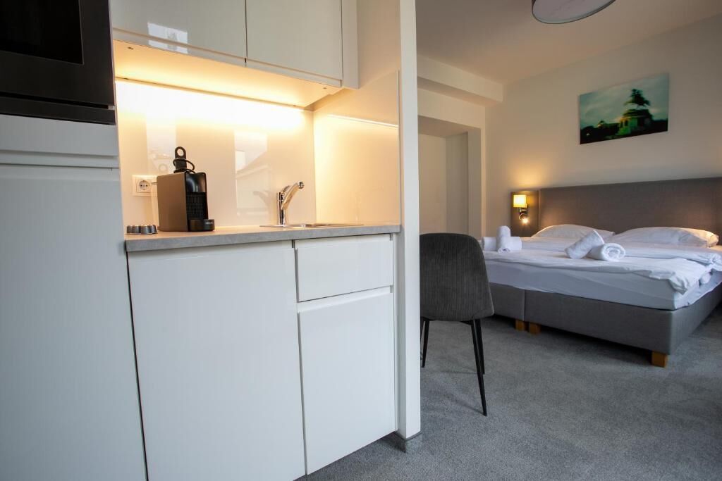 Ein Hotelzimmer mit einem Bett, einem Sessel, einem Schreibtisch mit Wasserkocher und einem Bild an der Wand.