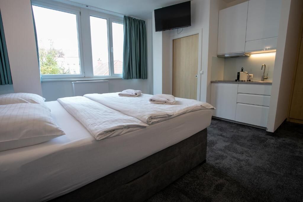 Ett hotellrum med en säng, en TV, ett litet kök och ett fönster.