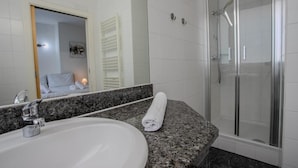 A bathroom with a white sink, a mirror, a towel, and a glass-enclosed shower. - Cube Apartments by Wiener Stadthalle (Vienna)
