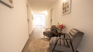 A hallway with a round rug, two grey armchairs, a small table, and a vase with flowers. - Cube Apartments by Wiener Stadthalle (Vienna)