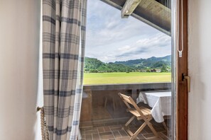 Ein Balkon mit Tisch und Stühlen, mit Blick auf eine grüne Landschaft mit Hügeln.