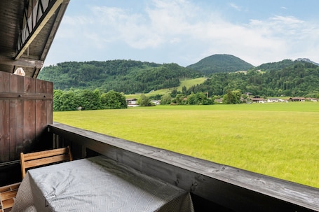 A wooden deck with a table and chairs overlooking a green field and mountains.. Studio Apartment 'Brünnsteinblick' with Mountain View and Balcony