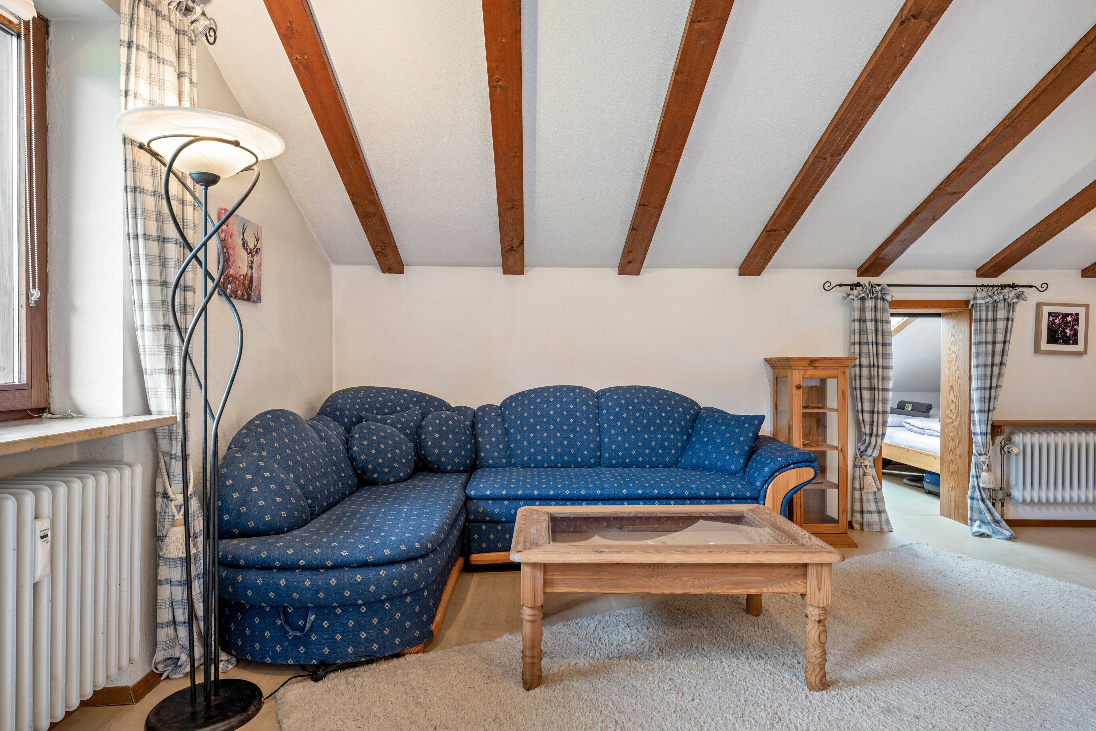 Ein gemütliches Wohnzimmer mit einem blauen Sofa, einem Holztisch, einer Stehlampe und einer Heizung.