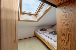 Una habitación pequeña con estructura de madera, tragaluz, cama individual y suelo de madera.