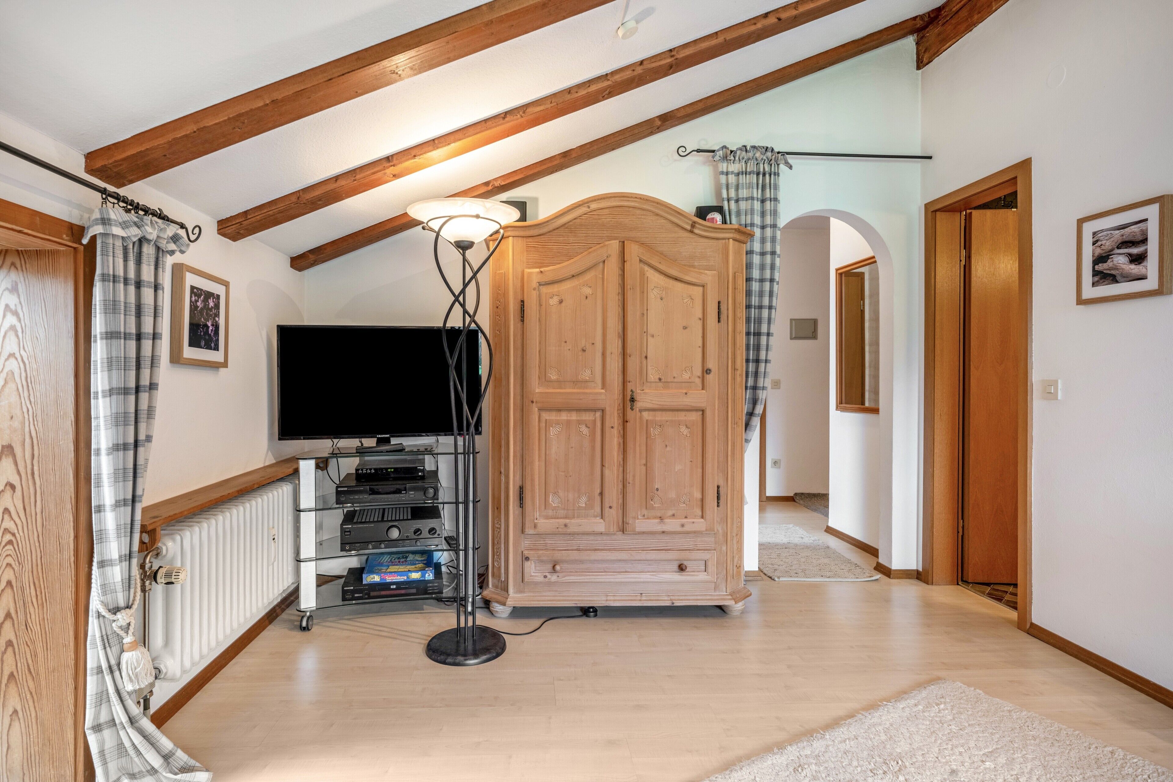 A room with a wooden ceiling, a television, a cabinet, and a radiator.