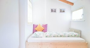 A bedroom with a wooden bed frame, white bedding, and two framed pictures on the wall.
