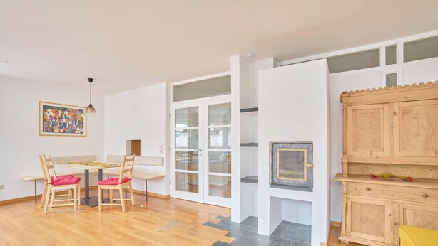 Una habitación con una mesa de madera, sillas, un banco, un armario y una puerta con paneles de vidrio.