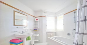 A bathroom with a sink, mirror, shower, and a shelf with towels.