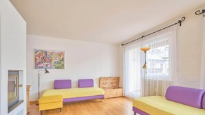 Una habitación con dos camas, un cofre de madera, una lámpara de pie y una ventana con cortinas.