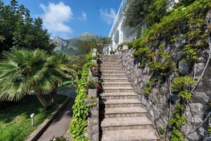 A stone staircase leading to a building with a white facade, surrounded by greenery and a mountainous backdrop. - Belvedere Apartment - Breathtaking sea view with terrace in Nerano (Nerano)