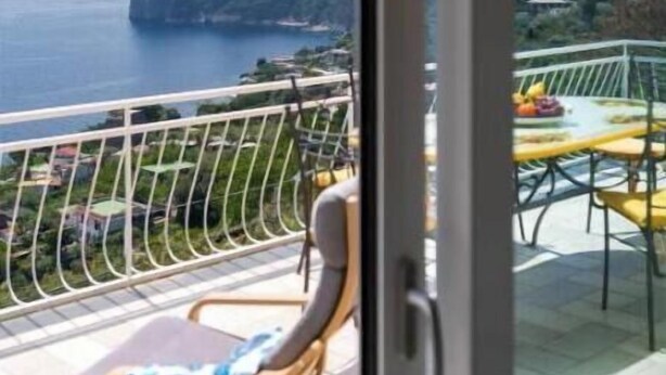 A balcony with a view of the sea and mountains, a table with chairs, and a hanging light fixture. - Belvedere Apartment - Breathtaking sea view with terrace in Nerano (Nerano)