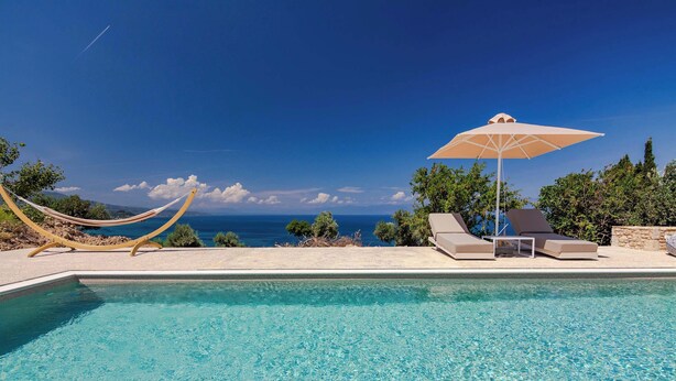Piscina cristalina con vistas al mar, una hamaca y sillas de descanso con una sombrilla.