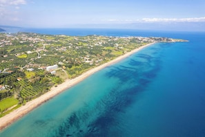 Vista aérea de una zona costera con playa, edificios residenciales y vegetación.