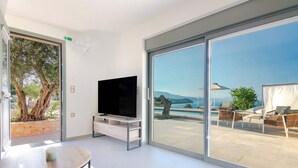 Habitación moderna con televisión, una mesa y un amplio ventanal corredero que da a un área exterior con piscina y sillas de descanso.