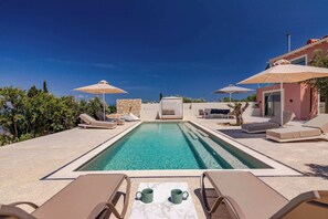A pool with lounge chairs and umbrellas, a stone wall, and a building with a red roof. - Assini Estate - Nestor Poolside Suite near Koroni (Koroni)