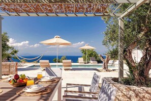 An outdoor dining area with a view of the sea, umbrellas, lounge chairs, and a hammock. - Assini Estate - Nestor Poolside Suite near Koroni (Koroni)