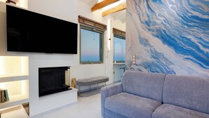En moderne stue med et fladskærms-tv, pejs, en grå sofa og et stort abstrakt vægmaleri.
