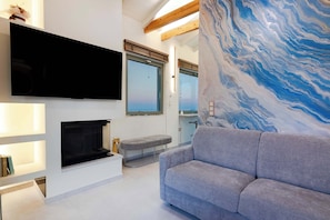 Una sala de estar moderna con un televisor de pantalla plana, una chimenea, un sofá gris y un amplio mural abstracto.