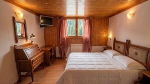 A wooden-paneled bedroom with a bed, a desk, a television, and a window with curtains. - Garnì Pirata (Cavareno)