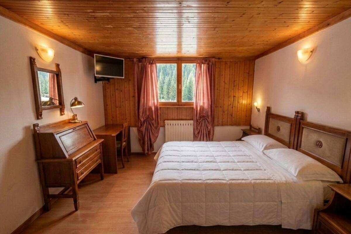 Un dormitorio con paneles de madera, una cama, un escritorio, un televisor y una ventana con cortinas.