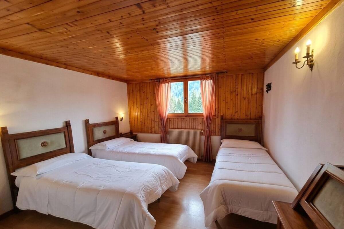 Una habitación con cuatro camas individuales, techo de madera, una ventana con cortinas y un radiador.