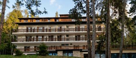 Un immeuble à plusieurs étages doté de balcons, entouré d’arbres.