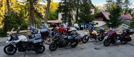Una fila de motocicletas estacionadas en un área de aparcamiento, con árboles y edificios al fondo.