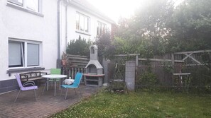 Eine Terrasse im Freien mit Tisch und Stühlen, einem Grill und einem Gartenbereich.
