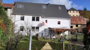 Ein zweistöckiges Haus mit Satellitenschüssel, einer Holzterrasse und einem umzäunten Garten.