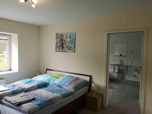 Ein Schlafzimmer mit einem Bett, einem Nachttisch, einem Wandbild und einem durch eine offene Tür einsehbaren Badezimmer.