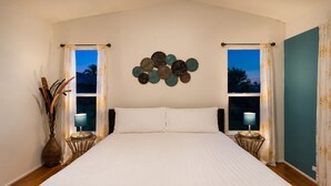 Ein Schlafzimmer mit einem großen Bett, zwei Nachttischlampen, einem Wanddekor und Blick aus dem Fenster.