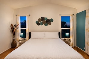 A bedroom with a large bed, two bedside lamps, a decorative wall piece, and a view through the window. - 25% Off June! Great 4 Families -Pool & Pool Table* (Bermuda Dunes)