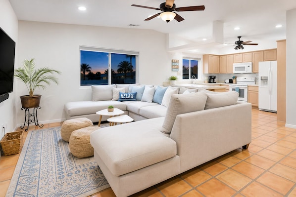 A modern living room with a sectional sofa, a flat-screen TV, a ceiling fan, and a kitchen in the background. - 25% Off June! Great 4 Families -Pool & Pool Table* (Bermuda Dunes)