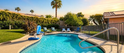 A swimming pool with a metal ladder, lounge chairs, and a palm tree in the background.