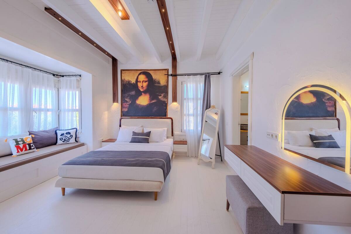 A bedroom with a bed, bedside table, and a large painting of the Mona Lisa.